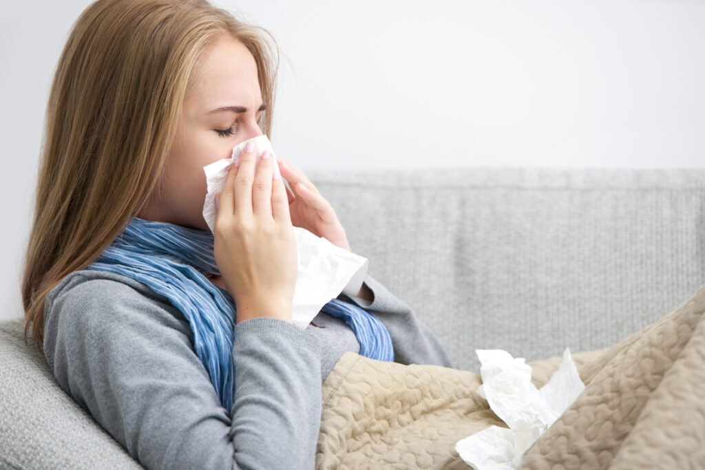 Close up of a young woman sneezing into a tissue while sitting on a couch.